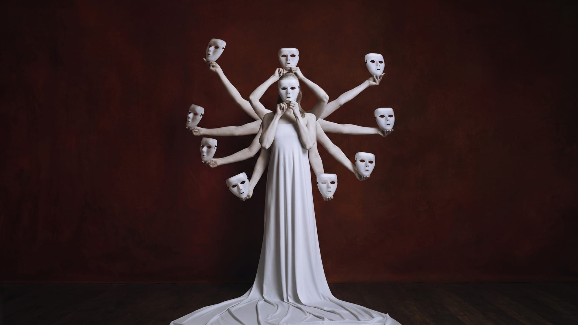 A woman in a white dress holds a mask to her face, surrounded by many white arms holding more white masks.